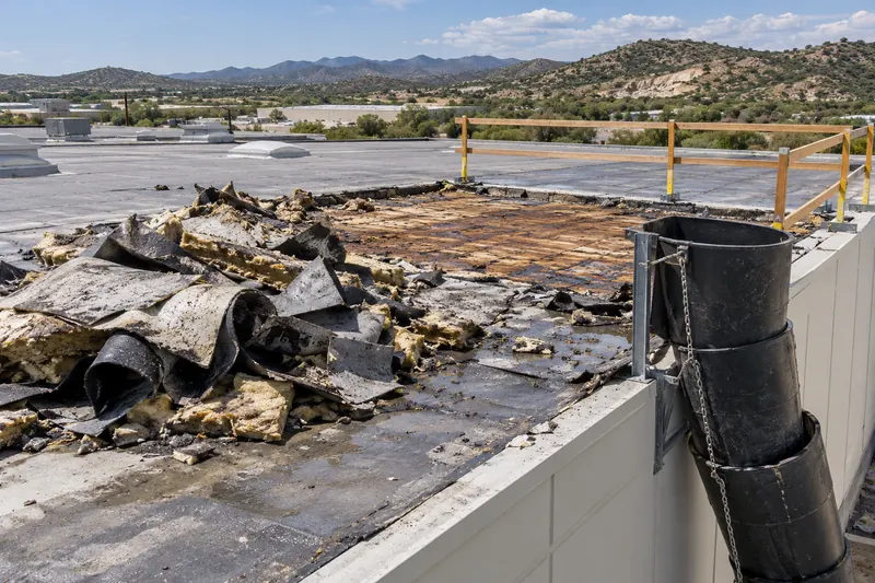 Torn-off roofing and wet insulation piled near a debris chute